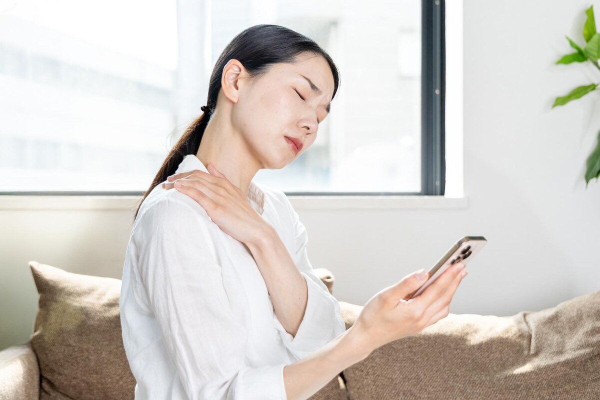 スマートフォンを見ながら首肩の重さを感じる30代女性｜揉んでも戻る首こりと頭の重さ